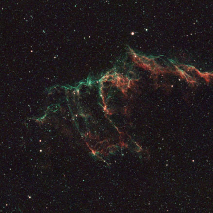 The arc-shaped veil of gas spanning this image is mostly green in the upper parts and red-orange in the lower parts